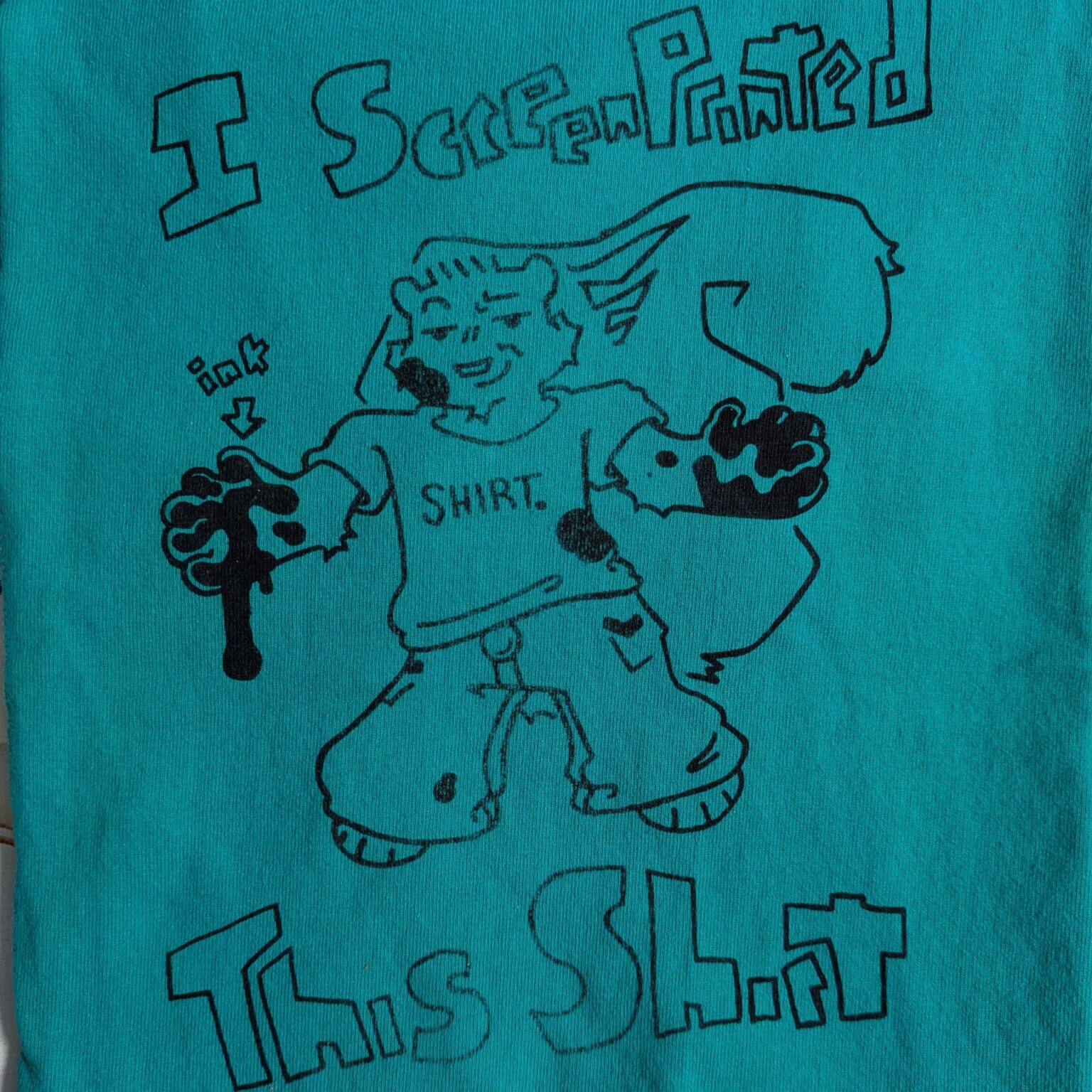 A screenprinted design on a green shirt. The design is a smug looking squirrel who's paws are a mess with ink. The text reads 'I screenprinted this shirt'